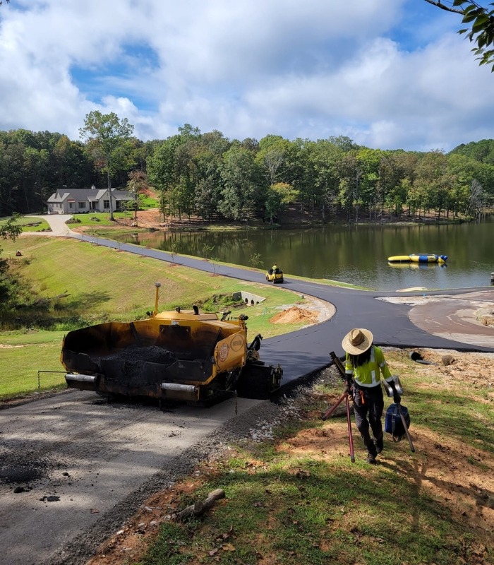 paving a long asphalt driveway next to pond