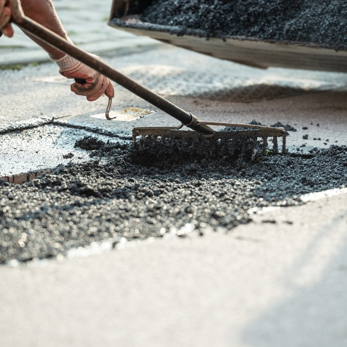 worker filling a pothole with asphalt